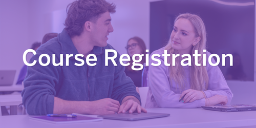 Two students sitting at a desk in a lecture room talking with one another