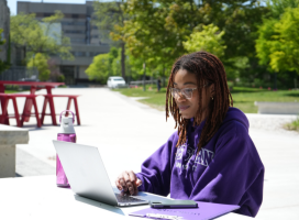 A student sitting on their laptop outside on campus